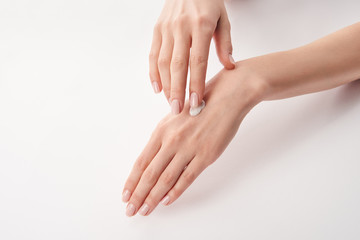 Partial view of woman applying cosmetic cream on white background