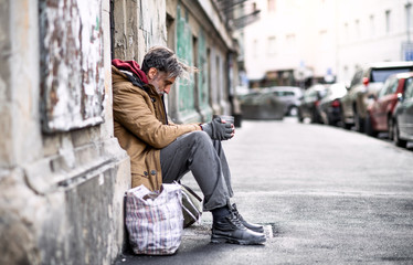 Homeless beggar man sitting outdoors in city asking for money donation. - obrazy, fototapety, plakaty