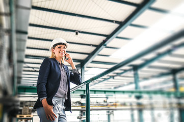 A portrait of an industrial woman with smartphone, standing in a factory.