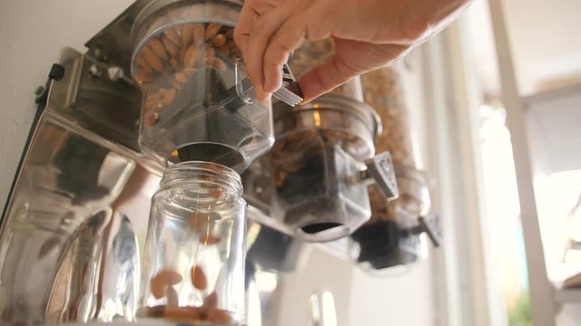 Young Woman Pours Raw Almond in Glass Jar. Vending Machine with Nuts and Grains in Zero Waste Shop. No plastic Conscious Minimalism Vegan Lifestyle Concept. 4K Slowmotion.
