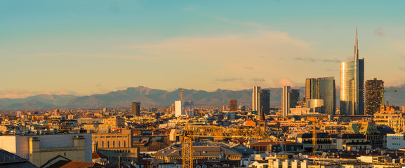 Obraz premium Widok na panoramę Mediolanu o zachodzie słońca z Alpami w tle.