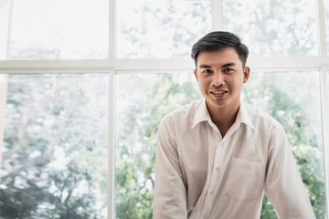 Portiat of Attractive Asian business man or university student positive person with happy face smiling looking at camera near windows on vacation time in summer day