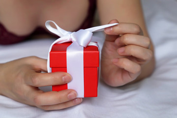 Valentine's day gift, sexy woman in underwear opens red gift box on the bed. Romantic morning, present in female hands close up, concept of birthday, anniversary, surprise