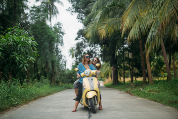 A pair of beautiful women travel by scooter through the jungle in Southeast Asia. Thailand