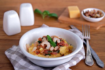 Homemade shrimp and grits with bacon, Chedder cheese and parsley in a white bowl on a wooden table.