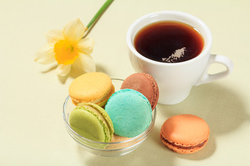 Cup of coffee and delicious macarons cakes of different color on plate.