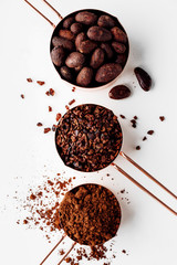 Rose gold measuring cups of cocoa beans, cacao nips and cocoa powder on a white background, flat...
