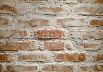 Real loft wall of red bricks decorated with white paint under hard vertical light. Background.