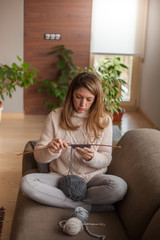 Beautiful woman sitting on the sofa of the living room and knitting for winter at home