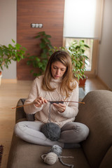 Fototapeta premium Beautiful woman sitting on the sofa of the living room and knitting for winter at home