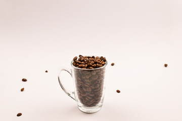 Grains of coffee are poured into a glass cup on a white background