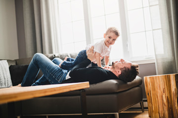 A Portrait of handsome father and his cute son having fun on sofa at home