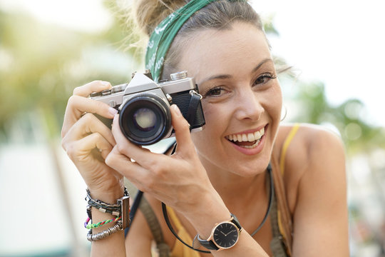 Portrait of stylish young woman taking photos with vintage camera in urban setting