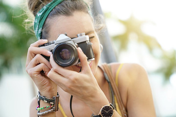 Portait of stylish young woman taking photos with vintage camera in urban setting