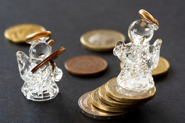 Glass angel figure over coins column on black background