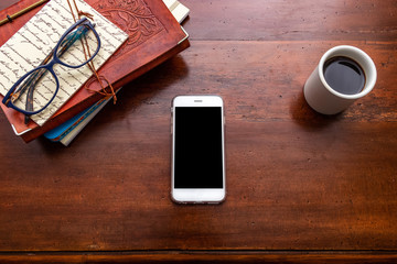 Smartphone on wooden table. Books and cup of coffee complete the image.