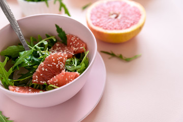 Fresh citrus salad with arugula, grapefruit and sesame seeds on pink background. Selective  focus. Raw vegetarian spring detox food.