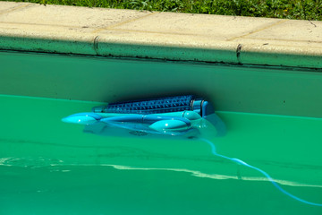 An automatic robot pool cleaner climbs the side of a cloudy swimming pool removing debris and algae