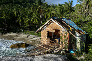 Old decaying bungalow type houses on beach rocks with palm trees in an abandoned tourist resort in Koh Phangan Thailand