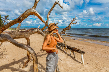 Girl in hat poses near dry tree on sea coast