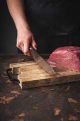 female hands cut raw pork on a wooden board in the kitchen