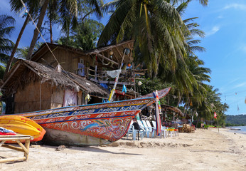Koh Phangan, Thailand - December 20, 2018: Beautiful colorful wooden fishing boat on a Tropical beach shore in Koh Phangan, Thailand with coconut palm trees and a small bungalow house