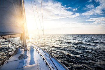 White yacht sailing at sunset. A view from the yacht's deck to the bow and sails. Baltic sea, Latvia - obrazy, fototapety, plakaty