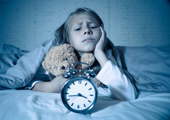 Little Girl in bed awake at night yawning and feeling restless showing clock she can not sleep