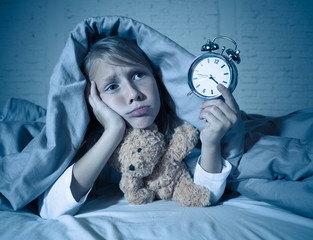 Little Girl in bed awake at night yawning and feeling restless showing clock she can not sleep
