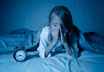 Little girl suffering from insomnia looking at alarm clock feeling desperate sad and restless