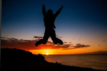 Silhouette of young boy jumping near the sea at the sunset Concept image of freedom and happiness of a teenager Teen jump with ocean and sunlight in background Postcard from a summer holiday vacation