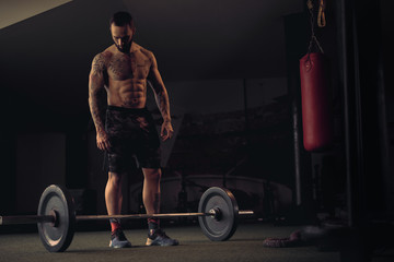 Shirtless tattooed athlete looking at the weights on the floor