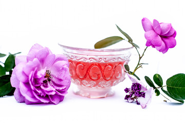 Close up view of organic fresh rose tea in a transparent glass cup isolated on white with raw roses.