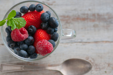 glass cup with berries, blueberries, raspberries, strawberries, and mint.On the wooden table light