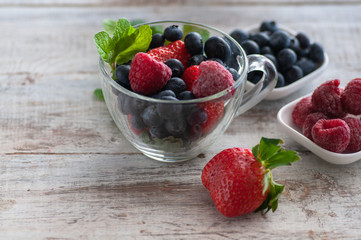 glass cup with berries, blueberries, raspberries, strawberries, and mint.On the wooden table light