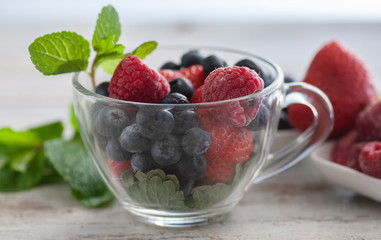 glass cup with berries, blueberries, raspberries, strawberries, and mint.On the wooden table light