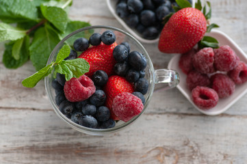 glass cup with berries, blueberries, raspberries, strawberries, and mint.On the wooden table light