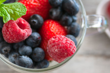 glass cup with berries, blueberries, raspberries, strawberries, and mint.On the wooden table light