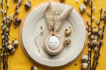 Happy Easter card. Cute egg in a napkin in the form of a bunny on a ceramic plate. Quail eggs. Happy Easter concept background
