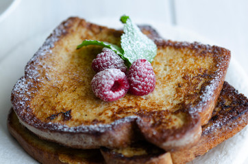 Close up of French toast, making with bread soaked in eggs and milk, then fried , served with icing sugar and raspberries with mint.