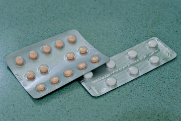 Two packages of pills on a teal surface