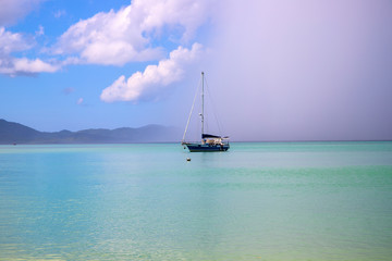 Sailing yacht in turquoise blue sea under rainy cloud. Tropical storm in marine lagoon. Rain cloud on exotic seashore