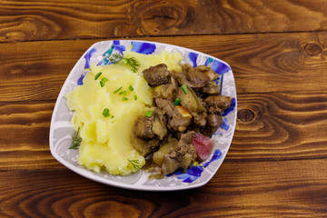Mashed potatoes with stewed chicken liver with apple and onion on wooden table
