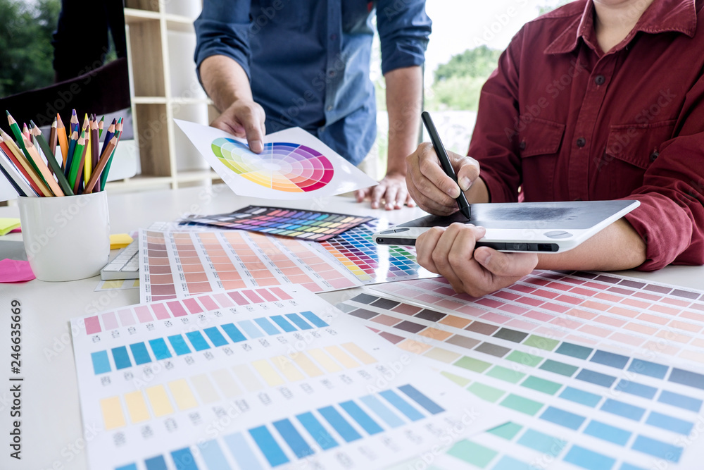 Poster Two colleague creative graphic designer working on color selection and color swatches, drawing on graphics tablet at workplace with work tools and accessories