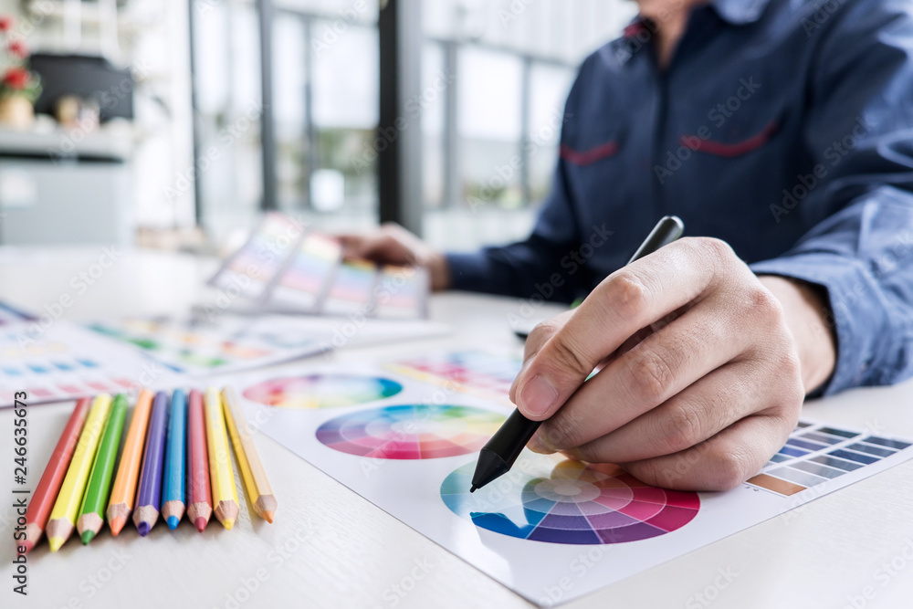Poster Image of male creative graphic designer working on color selection and drawing on graphics tablet at workplace with work tools and accessories