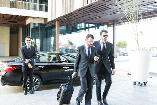 Businessman With Luggage Walking By Bodyguard