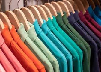 Colorful polo shirt on hang for sale in shop. Green blue polo on wooden hanger. Summer season wear in department store