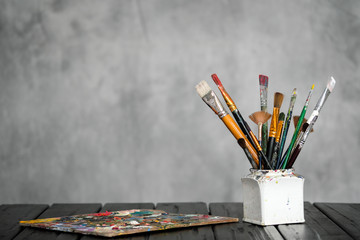 Artist's tools, brushes, paints and a palette lie on a black wooden table on a gray fabric...