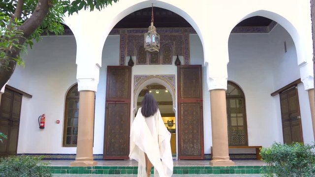 Beautiful Moroccan Girl Waving her light white mantle in Picturesque Dar Si Said Riyad in Marrakech at sunset time