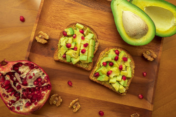 Two Avocado Toasts with pomegranate seeds on a wooden tray